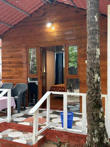 a log cabin with a porch and a tree at Coconut Grove Palolem in Canacona