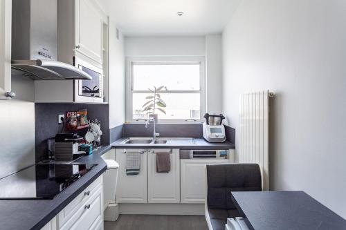 une cuisine avec des armoires blanches, un évier et une fenêtre dans l'établissement Appartement Neuilly, à Neuilly-sur-Seine
