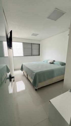 a white bedroom with a bed and two windows at Apto Guaruja in Guarujá