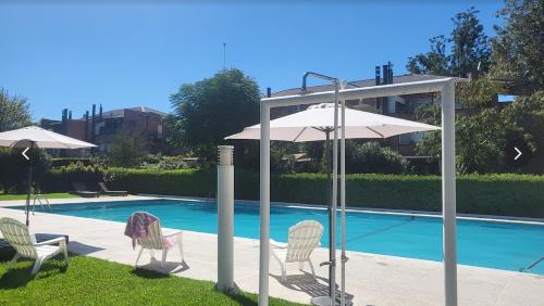 a group of chairs and an umbrella next to a pool at Muy buen apartamento con parrilla y piscina, en country in Pilar