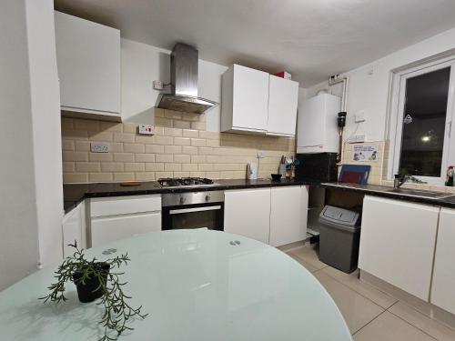 a kitchen with white cabinets and a table in it at Rooms Near Canary wharf in London
