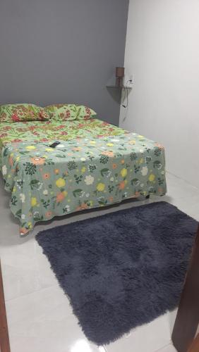 a bed with a green blanket with flowers and a rug at Flat Brisa do Mar in Pitimbu