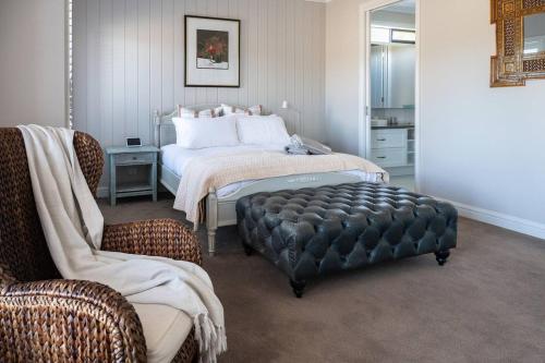 a bedroom with a bed and a chair and a ottoman at Bundjil Beach House Inverloch in Inverloch