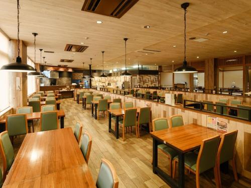 a restaurant with wooden tables and green chairs at Sagayamato Onsen Hotel Amandi in Saga