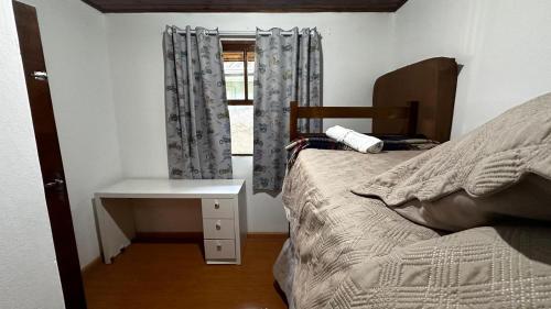 ein Schlafzimmer mit Bett, Schreibtisch und Fenster in der Unterkunft Solar Campos do Jordão - Perfeita para casal e Família in Campos do Jordão