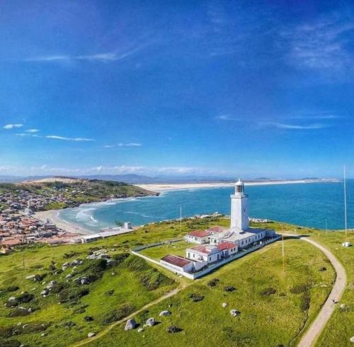 a lighthouse on a grassy hill next to the ocean at Apartamento aconchegante Mar Grosso in Laguna