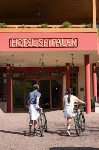 two people walking their bikes in front of a hotel sprinkler at Hotel Spitaler in Appiano sulla Strada del Vino