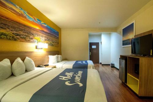 a hotel room with two beds and a flat screen tv at Days Inn & Suites by Wyndham Houston North/Aldine in Houston