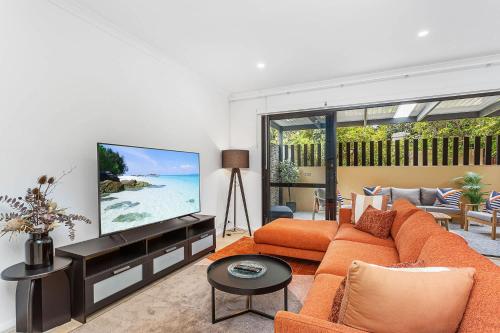 a living room with an orange couch and a flat screen tv at Renovated Townhouse in Northbridge in Perth
