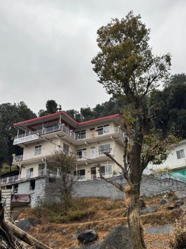 a building on a hill with a tree in the foreground at Paradise Inn by HBR in Dharmsala