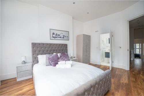 a white bedroom with a large bed with purple pillows at Stunningly Luxurious London Apartment (MHB350) in London