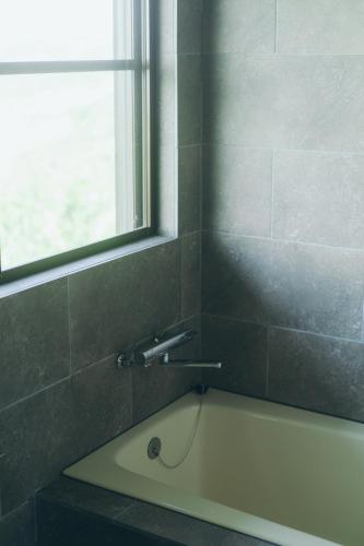 une baignoire dans une salle de bain avec une fenêtre dans l'établissement Atelier Hyakuna, à Nanjō