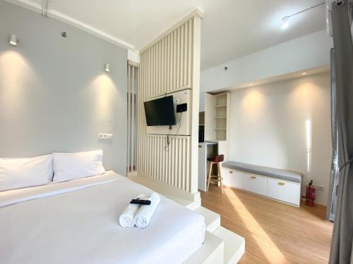 a white bedroom with a bed and a tv at Homey and Elegant Studio Vasanta Innopark Apartment By Travelio in Cikarang