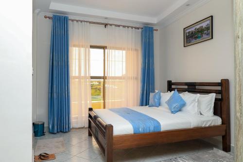 a bedroom with a bed with blue curtains and a window at Shanvilla Resort Ltd in Murangʼa