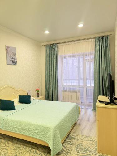a bedroom with a bed and a television and a window at ЖК Орлеу 2 комнатная in Karagandy