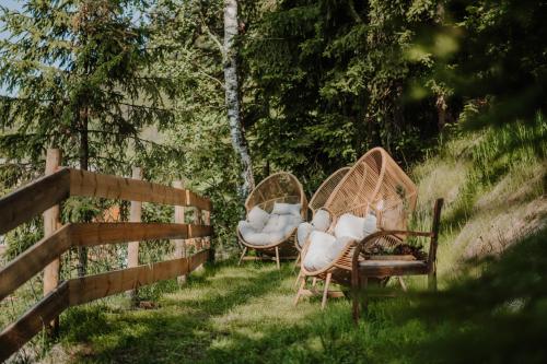 two wicker chairs sitting in the grass next to a fence at Hotel Berghaus Rosengarten in Nova Levante