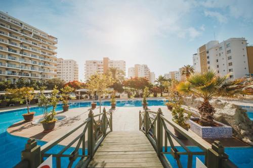 a wooden walkway leading to a swimming pool with buildings at Ground Garden View Apartments in Caesar Resort & SPA, Long Beach in Perivolia tou Trikomou