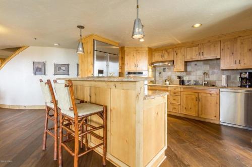 a kitchen with wooden cabinets and a bar with two chairs at Grand Summit Hotel #702 Penthouse Ski-In, Ski-Out Corner Unit in Park City