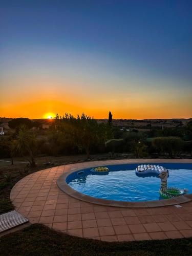 a swimming pool with a sunset in the background at Pôr-do-sol Villa in São Pedro do Corval