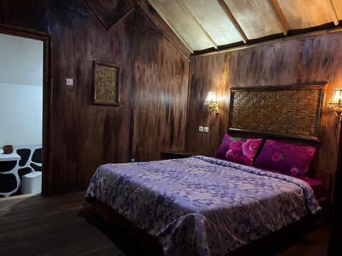 テテバトゥにあるSyaqila Homestay Lombokの木製の壁のベッドルーム1室、紫色のシーツが備わるベッド1台が備わります。