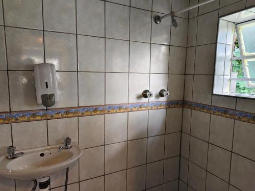 Un baño de azulejos blancos con lavabo y ventana. en CradleLicious camp & caravan, en Beckedan