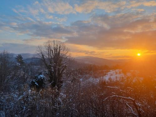 a sunset over a snowy field with the sun in the sky at Cosy home D&D in Brod Moravice