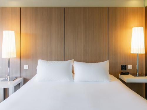 a large bed with white pillows and two lamps at Pullman Bordeaux Lac in Bordeaux