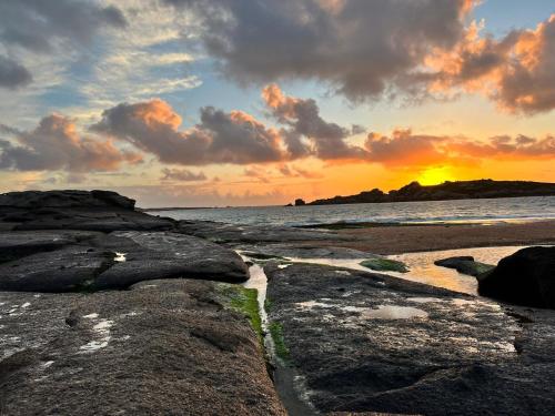 a sunset over the ocean with rocks on the beach at Environnement calme et reposant - Côtes-d'Armor in Ploëzal