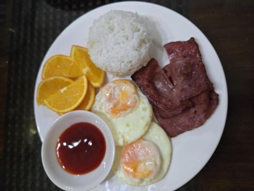 a plate of breakfast food with eggs meat and oranges at Jex Poolpoint Villa in El Nido
