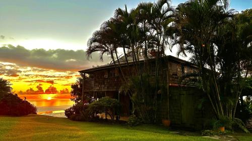 a house with palm trees in front of a sunset at Habitation Caféière Samana Beauséjour - GUESTHOUSE in Pointe-Noire