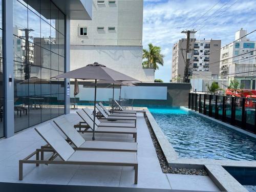 a pool with lounge chairs and an umbrella on a building at Apartamento 100m da Praia Brava - Itajaí in Itajaí