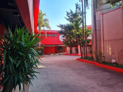 a red building with palm trees in front of a sidewalk at Impulse Motel in São Bernardo do Campo