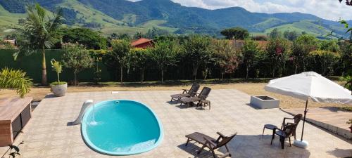 a swimming pool with chairs and an umbrella on a patio at Chalé de alto padrão em condomínio in Santa Rita do Sapucaí