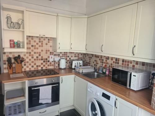 een keuken met witte kasten en een wasmachine en wastafel bij Spacious two bedroom flat, central location in Plymouth