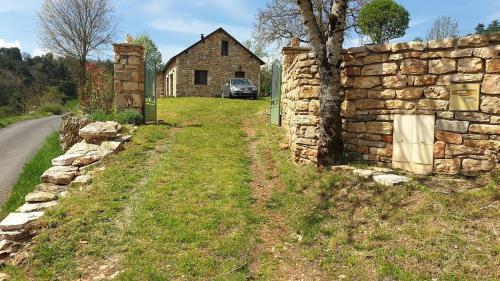 un mur en pierre à côté d'une maison avec une voiture dans l'établissement Maison en pierre Gorges du Tarn, à Saint-Georges-de-Lévéjac