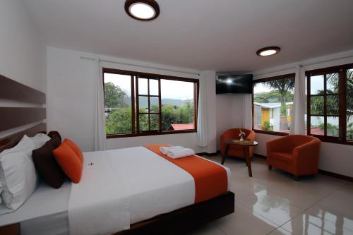 a bedroom with a bed and a chair and windows at La Posada de Mindo in Mindo
