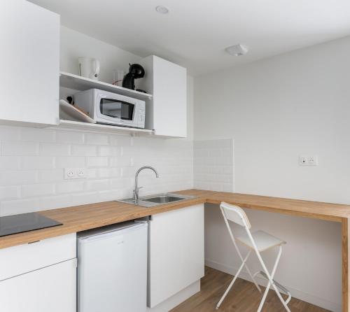 La cuisine est équipée de placards blancs, d'un évier et d'une chaise. dans l'établissement Dame Blanche, à Brest