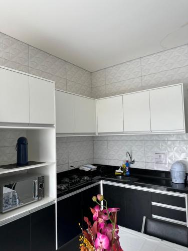a kitchen with white cabinets and pink flowers on the counter at Apartamento completo ate 5 pessoas ou um quarto com sala e cozinha para 2 pessoas in Sinop