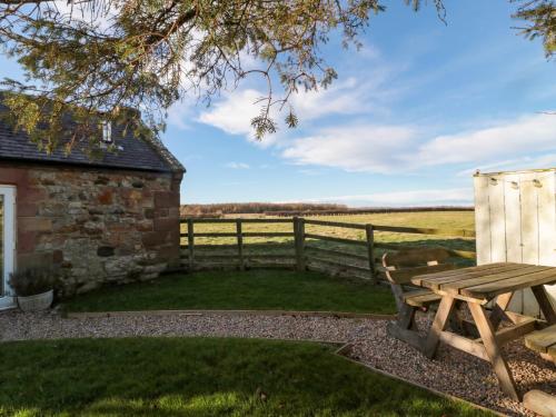 a wooden picnic table next to a fence and a field at The Forge in Chathill