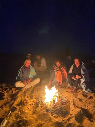 a group of people sitting around a fire on the beach at Art Of Balance in Tamraght Ouzdar