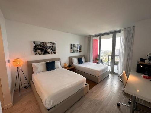 a bedroom with two beds and a desk and a window at Miami Apartment 2 Full beds with Beach service, pool and gym 2007 in Hallandale Beach