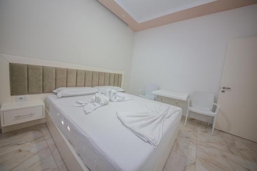 a white bedroom with a white bed and a table at Hotel Landi in Ksamil