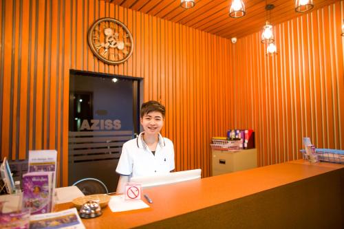 ピサヌロークにあるAziss Boutique Hotel - SHA Plusの橙室のカウンターの後ろに立つ女性