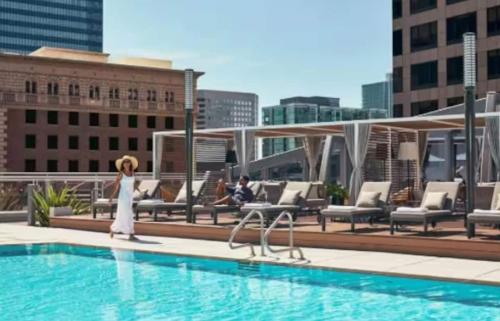 a woman standing next to a swimming pool on a building at Stunning 3 Bedroom High-Rise with Pool, Spa, and Rooftop Views in Los Angeles