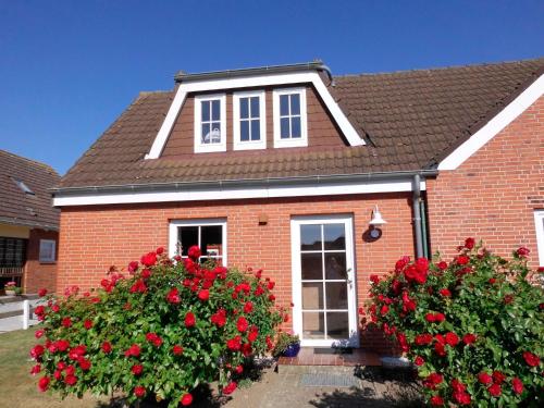 Una casa de ladrillos rojos con flores rojas delante de ella. en Appartement Klahn Nr1, en Fehmarn