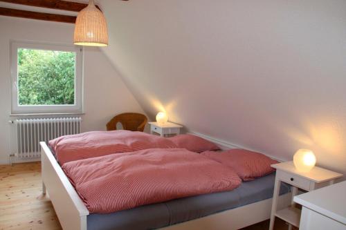 Schlafzimmer mit einem Bett mit rosa Bettwäsche und einem Fenster in der Unterkunft "Ferienhaus Strandläufer" in Neue Tiefe Fehmarn