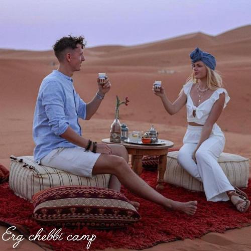 Ein Mann und eine Frau sitzen in der Wüste und halten Weingläser. in der Unterkunft Erg Chebbi Camp in Merzouga