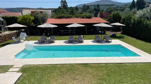 a swimming pool with chairs and umbrellas in a yard at Casa da Ponte de Mucela in Vila Nova de Poiares