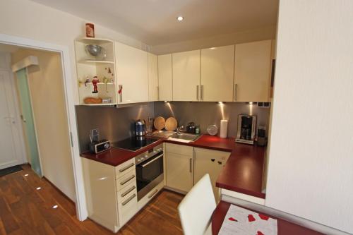 een kleine keuken met witte kasten en rode aanrechtbladen bij Strandidyll, 54 - Typ A1 in Grömitz