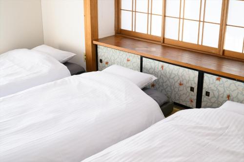 two beds in a room with white sheets at 玉造和暖 WaDan 島根県玉造温泉街に佇む和の趣あふれる古民家旅館 supported by COCOSTAY in Matsue